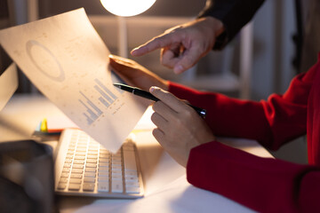Business team working overtime analyzing financial data in office at night. Two business professional are working overtime in the office, analyzing financial data and discussing strategy for success.