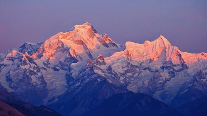 Panorama of snow covered mountain range glowing pink under alpenglow at twiligh