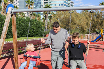 Father walking with teenager and toddler sons at a playground