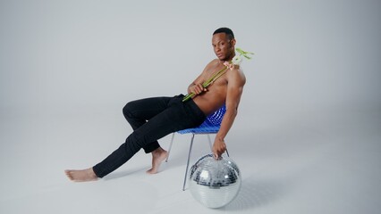 A performer showcases his artistic flair while seated on a chair, holding a flower. The atmosphere...