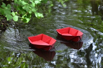 Two red origami boats on a still waterway