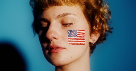 A young person stands still with eyes closed, showcasing a painted American flag on their face.