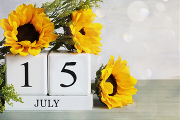 White wood calendar blocks with the date July 15th and beautiful sunflower bouquet with bokeh. Selective focus with blurred background. 