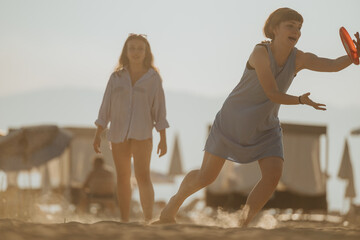 Two women sharing fun moments on the beach while playing frisbee under a sunny sky.