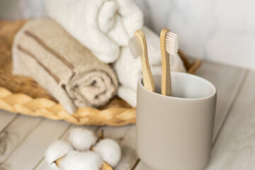 Minimalist eco bathroom scene with bamboo toothbrushes in glass and soft towels on light wood. Clean natural hygiene products for sustainable and zero waste lifestyle.