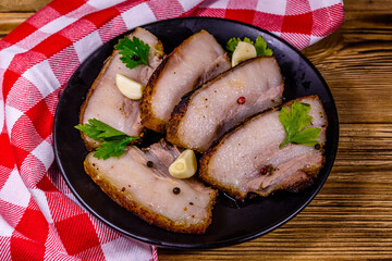 Slices of baked pork belly, garlic and parsley on a black plate
