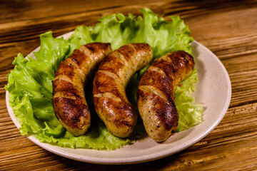 Plate with roasted sausages and lettuce leaves on a wooden table