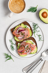 Smoked salmon avocado sandwich on light background. Black whole grain bread, avocado, salted salmon and dill for healthy breakfast