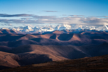 A snowy mountain range rolling hills dramatic sky sunlight natural landscape serene remote wilderness outdoor scenic view. sunlight highlights peaks creating peaceful and awe inspiring atmosphere
