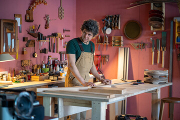 Professional pensive woodworker pauses to visualize project next to prepared wooden pieces. Workshop organization, handmade furniture production, creative manual labor job, material calculation