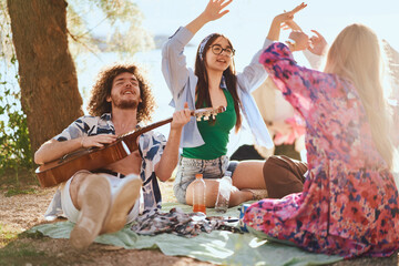 Fototapeta premium A group of friends and tourists enjoy a carefree moment on the beach at sunset, dancing, playing guitar, and celebrating together in a vibrant and joyful atmosphere.
