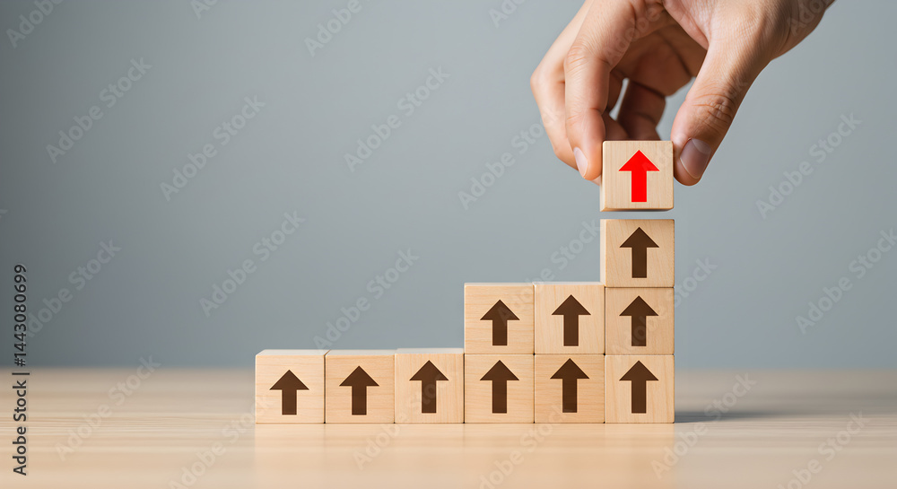Poster hand placing wooden block with red arrow on top of stack symbolizing growth on gray table