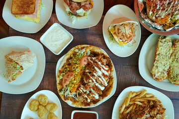 A table with many plates of food including sandwiches, wraps, and fries. There are also some condiments and a bowl of salad