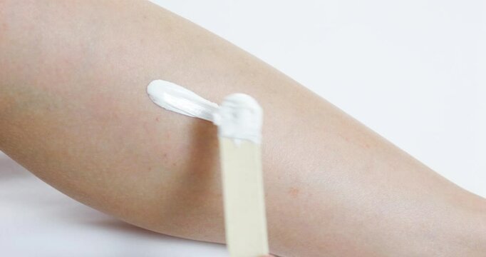 Warm sugaring paste applying on woman's leg with wooden spatula, professional beautician removing hair for smooth, silky skin during cosmetic procedure
