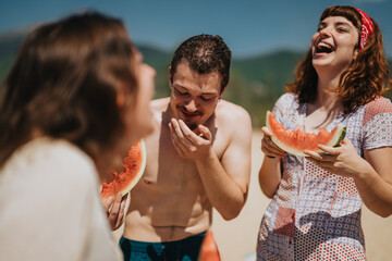 A joyful gathering of friends enjoying fresh watermelon on a sunny day by the lake. The cheerful...