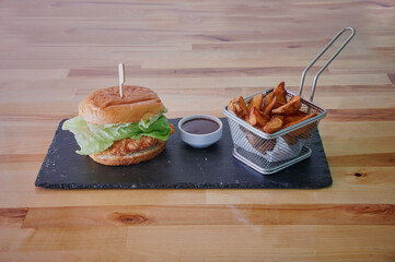 A burger with lettuce and a side of fries. The fries are in a basket. The burger is on a black plate