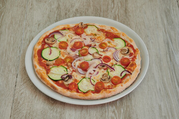 A pizza with vegetables on it is sitting on a white plate. The pizza has onions, tomatoes, and cucumbers