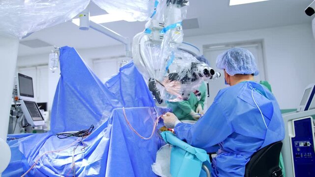 Distancing from a doctor sitting at microscope. Rear view of the neurosurgeon performing operation on brain.