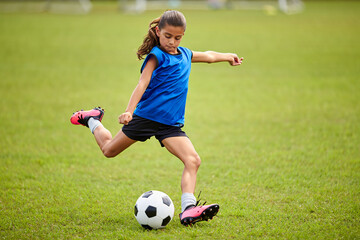 A child in a blue jersey kicks a soccer ball on a grassy field.