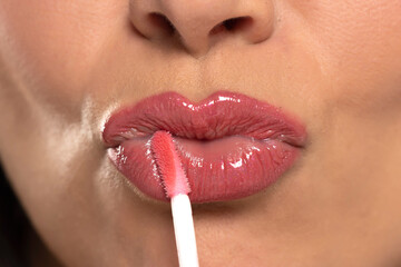 Close up woman applying pink moisturizing lip gloss . Perfect makeup.