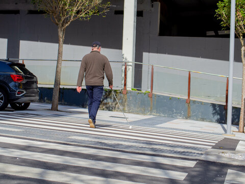 A sightless man walking on the crosswalk using his guide cane