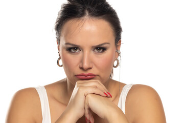Pensive woman with dark hair in white tank top, hand on chin, looking thoughtful. Serious...