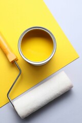 Can of yellow paint and roller on color background, flat lay