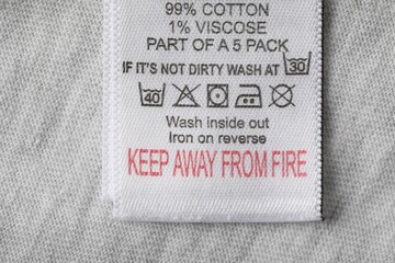 Clothing label with material content and care symbols on grey garment, top view