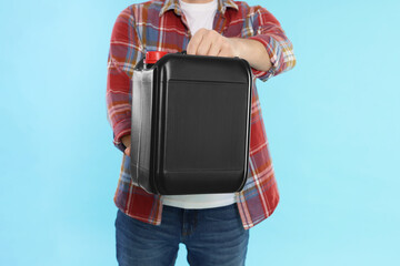Man holding plastic canister on light blue background, closeup