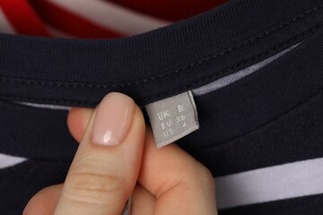 Woman holding clothing label of striped garment, closeup