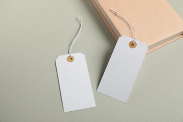 Blank tags with strings and book on grey background, above view
