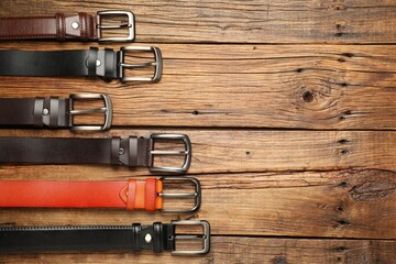 Many different leather belts on wooden table, flat lay. Space for text