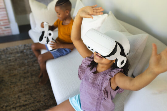Playing African American siblings exploring VR on sofa at home, with VR headset and controllers