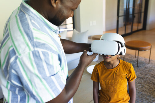 African American father and son trying on white VR headset in living room, with area rug