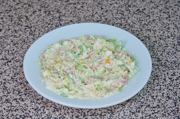 A white plate with a salad on it. The salad is made of lettuce, cheese, and ham