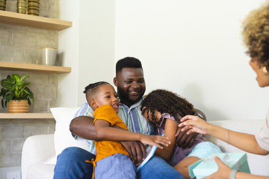 Diverse family reading together in living room on white sofa, with tablet and gift box