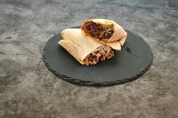 Two burritos on a black plate. One is open. The other is closed. The plate is on a gray surface