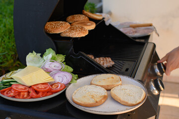 Homemade burgers being prepared on an outdoor grill at a countryside house. Juicy beef patty sizzling, sesame bun, fresh veggies, tomato ketchup, and cheese—perfect backyard cooking moment.