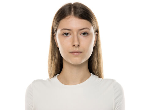 Close-up portrait of young woman with long straight light brown hair wearing white top, neutral expression, against white background, natural beauty, no makeup - Powered by Adobe