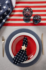 Table setting for USA Independence Day. Festive dinner with red plate and decoration in USA national flag colors and stars. Copy space. Vertical. View from above