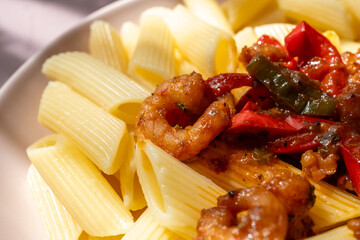 Close-up of penne pasta with shrimps on a plate, Mediterranean style with tomatoes