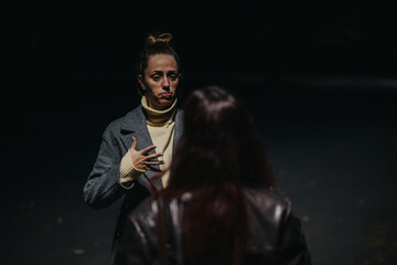 A candid scene of two women engaged in a nighttime conversation under dramatic lighting outdoors.