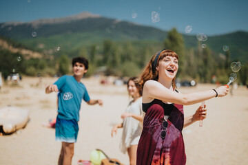 Friends spend time together outdoors at a sunny beach, playing and blowing soap bubbles. Capturing moments of joy, laughter, and summer fun surrounded by picturesque mountain scenery and golden sand.