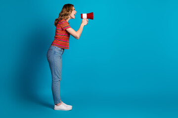 Young woman in casual outfit with megaphone against blue background expressing enthusiasm and...