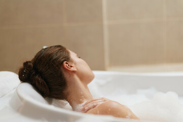 Relaxed woman enjoying a bubble bath in a modern bathroom, soft light creating a serene atmosphere, with focus on self-care and tranquility.