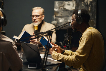 People in headphones sitting at table during podcast and discussing plot of new book together
