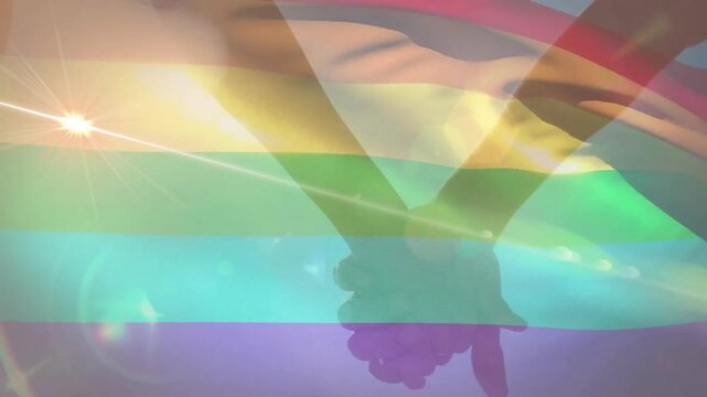 Clasped silhouette hands radiating unity in flat style with rainbow pride stripes and sunburst glow