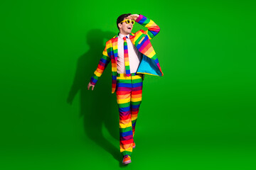 Charismatic young man in a vibrant rainbow-striped suit posing against a green background, radiating fun, energy, and pride