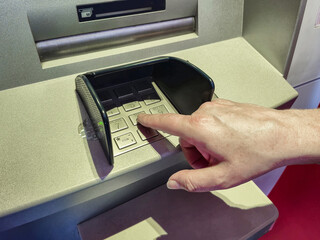Woman using ATM holding wallet an pressing the PIN security number on the keyboard automatic teller...