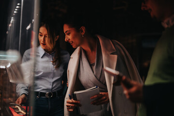 Two women observe museum exhibits with curiosity, one holding a notebook.